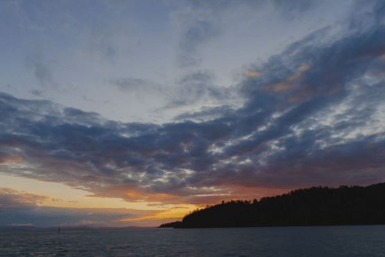 a sunset over a body of water with a mountain in the background