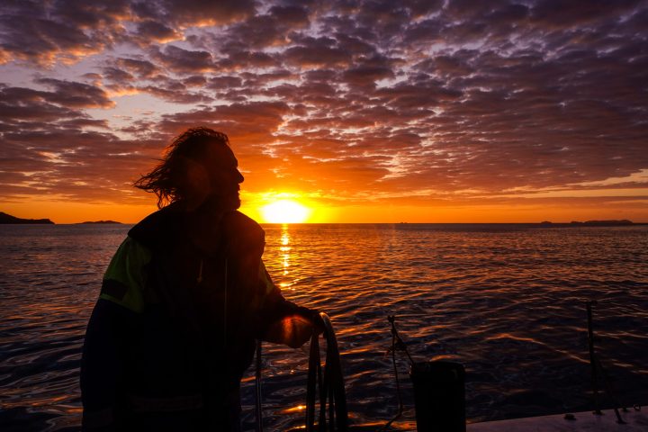 a man standing in front of a sunset over a body of water