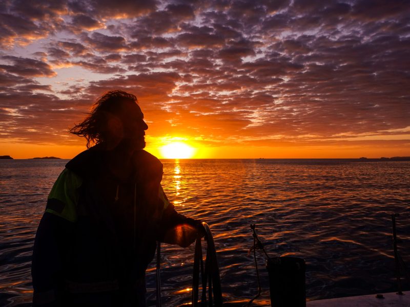 a man standing in front of a sunset over a body of water