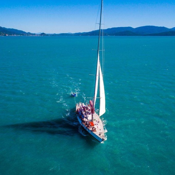 Sailboat with white sails on a calm ocean near distant hills under a clear blue sky.